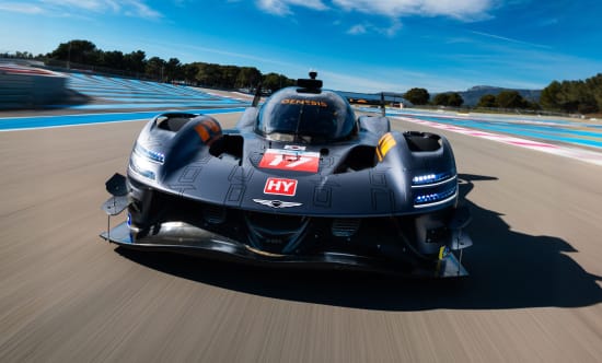 Front view of the GMR-001 hypercar racing on a circuit under a blue sky