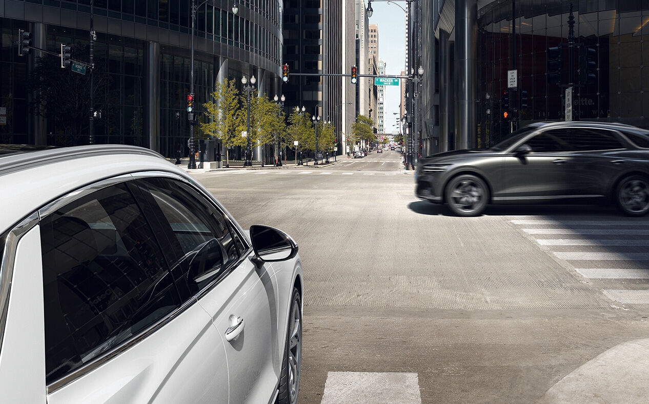 The Electrified GV70 is about to drive through a crossroads as another car speeds across.