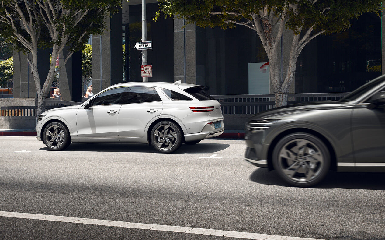 The Electrified GV70 is parked on the street as another car passes by from behind.