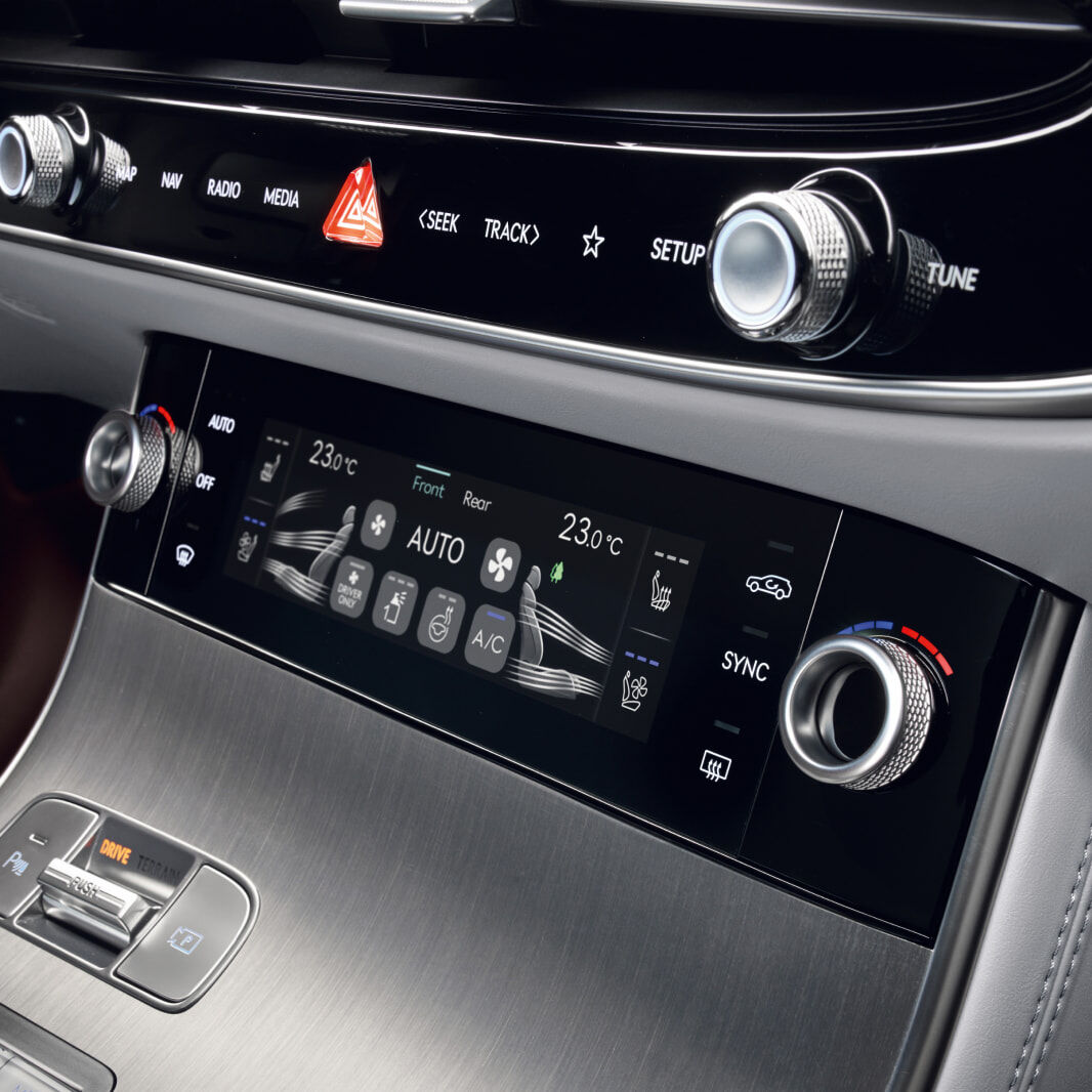 A view of the control panel in the front of the vehicle, featuring touch screens and dials that control ventilation and temperature.