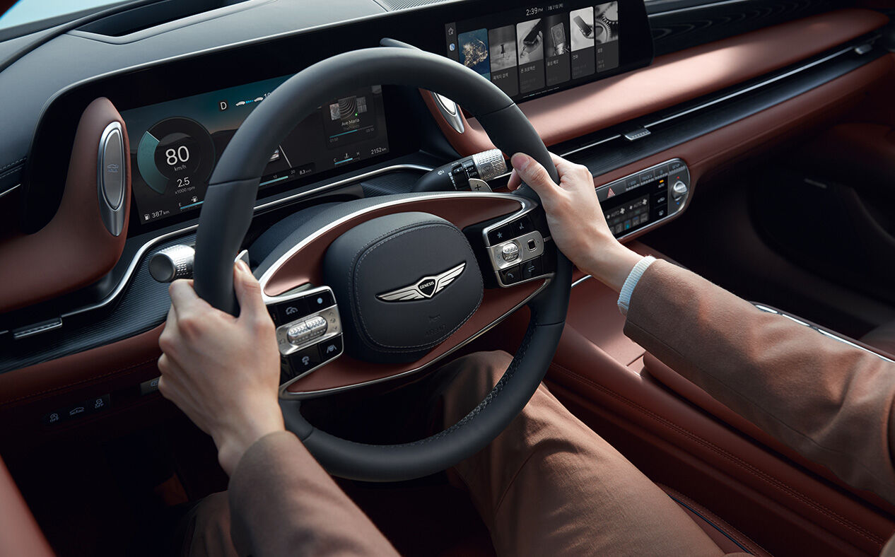 Hands hold the steering wheel in Bordeaux Brown interior.
