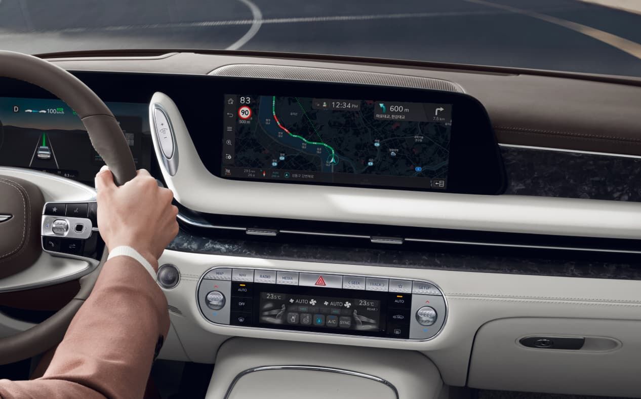 The driver holds the steering wheel and navigation is visible on the infotainment display in Glacier White interior.