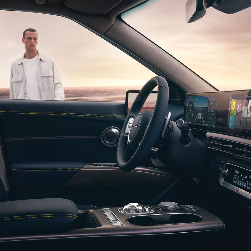 From the front seat of the GV60, you can see the spacious interior space of Genesis, and a man is walking towards the car.