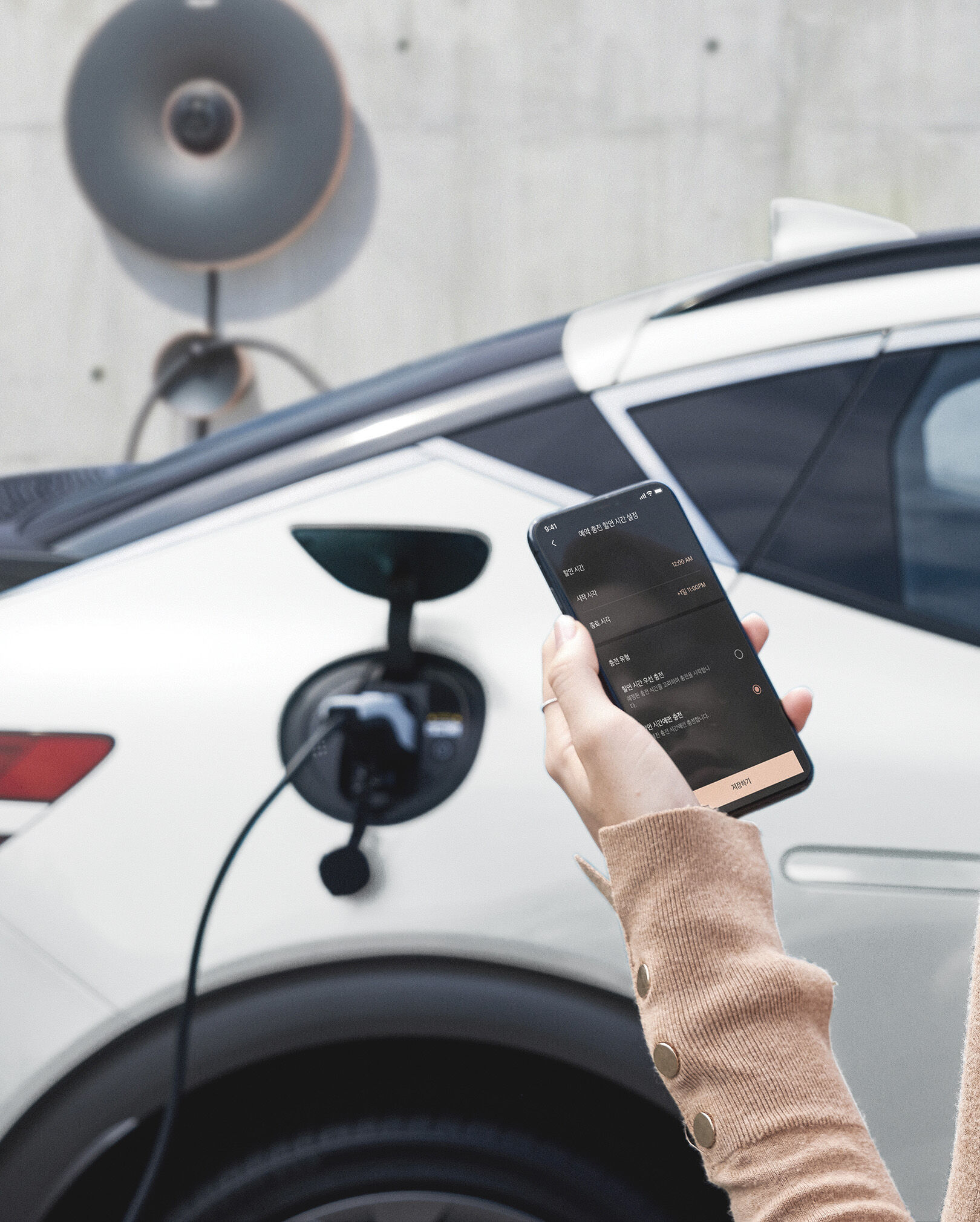 A driver looking at the My Genesis app and the GV60 vehicle being charged.