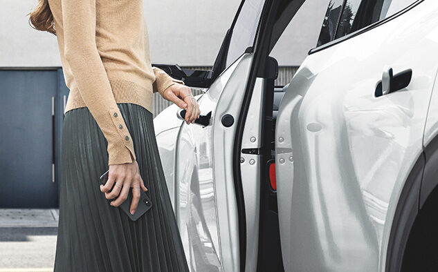 A driver holds a smartphone in one hand and opens the car door with the other.
