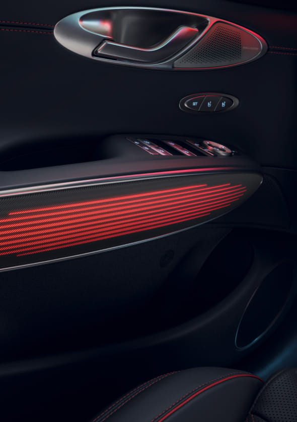 You can see the mood lighting in red on the interior door handle of the GV70 Sports Package. Above it are the door handle for opening and various control buttons.