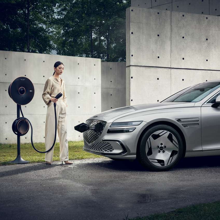 A G80 EV watches on at the side profile of a Genesis G80 in motion at a signal.