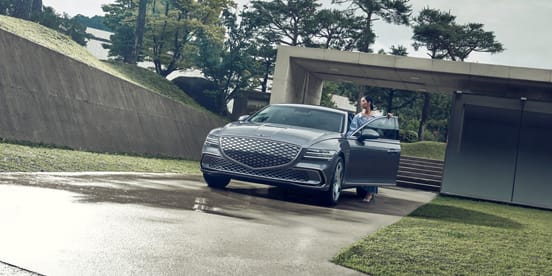 A Savile silver Genesis G80  EV switching lanes to join a Tasman blue G80 
