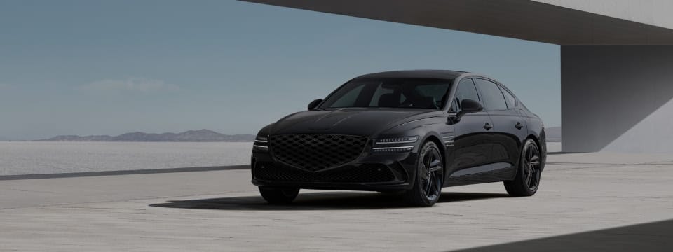 Genesis G80 luxury sedan in an elegant black finish, parked in front of a modern concrete backdrop.