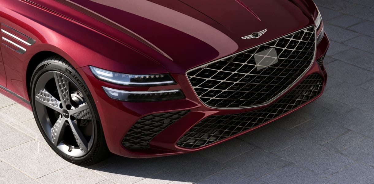 Close-up view of the Genesis G80’s front end, showcasing its bold grille, sleek headlights, and stylish alloy wheels.