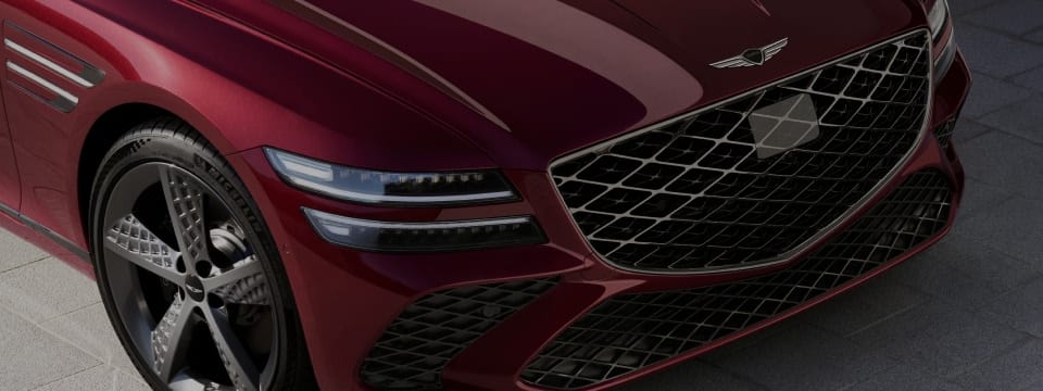 Close-up view of the Genesis G80’s front end, showcasing its bold grille, sleek headlights, and stylish alloy wheels.