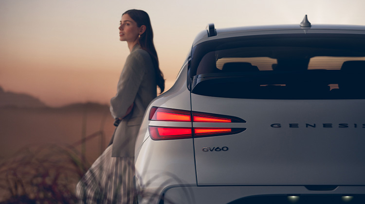 Rear camera view of white GV60 with female talent leaning on the left side of vehicle.