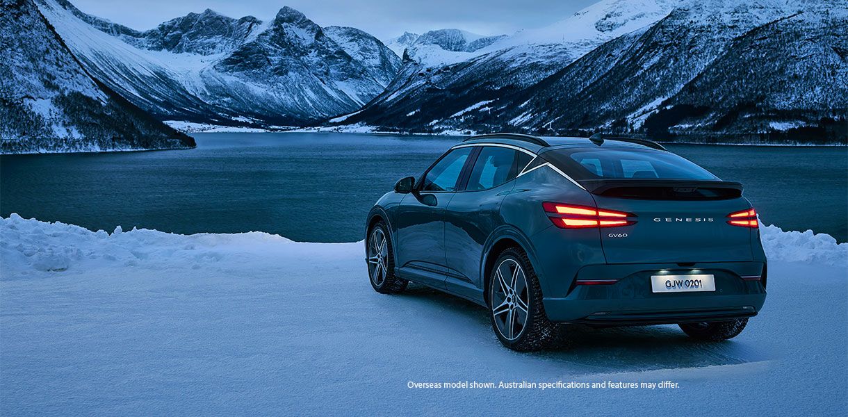 Genesis GV60 electric SUV parked on a frozen lakeside with snow-covered mountains in the background