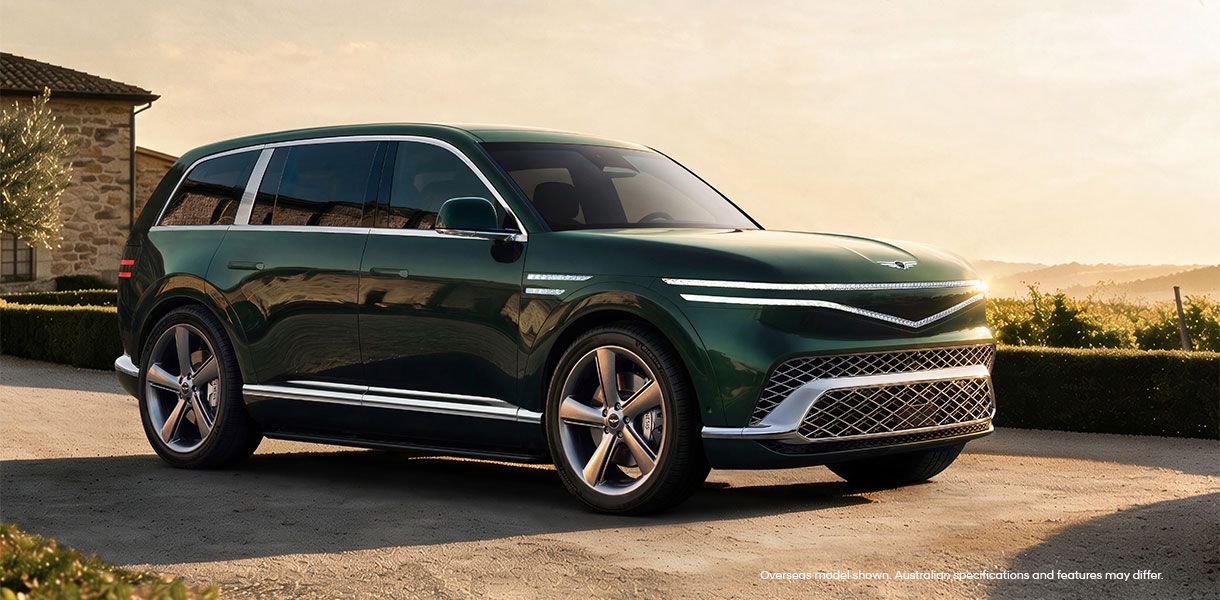Genesis GV90 luxury electric SUV finished in deep green, showcasing elegant design, signature two-line LED lighting, premium craftsmanship and refined performance in a sophisticated outdoor setting.