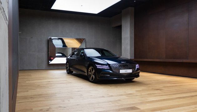 A calm-looking studio with light wooden floors, flattering overhead lighting and a sparkling car on display