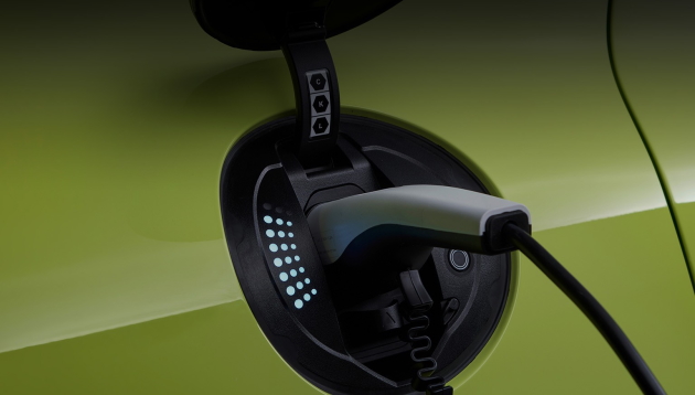 An electric charging plug sits in a lime green Genesis, futuristic LEDs light up to indicate the charging level