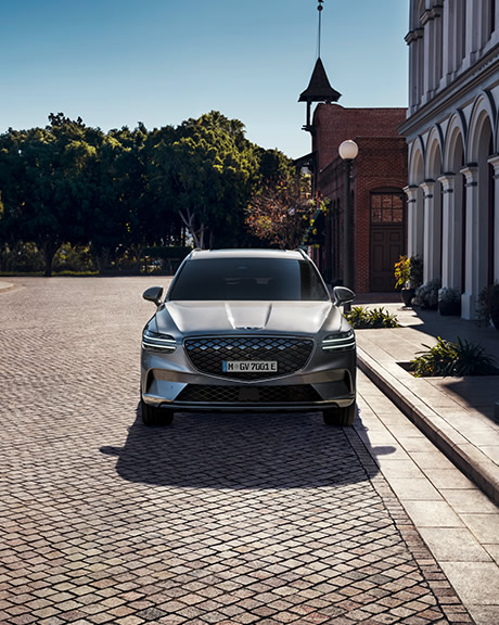 In a sunny cobbled courtyard a silver Genesis is parked. The afternoon sun reflects off its gleaming paintwork. 