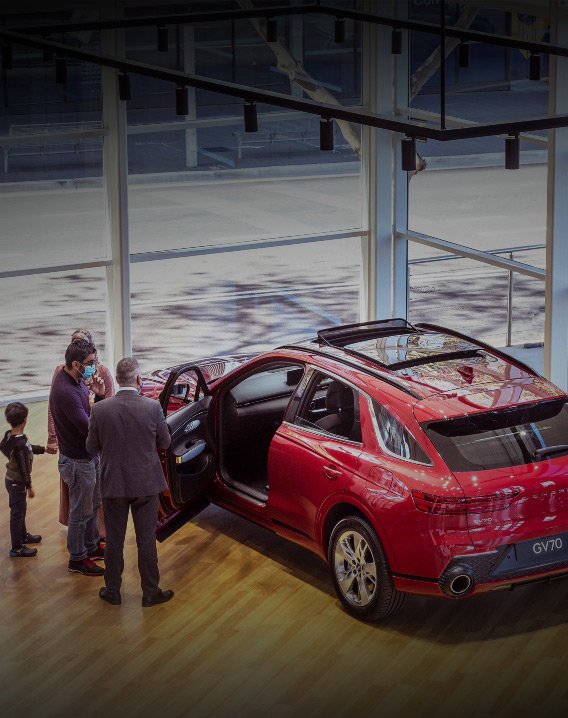 Family with young toddler and salesman inspecting a red gv70, opening the front passenger seat at a show room