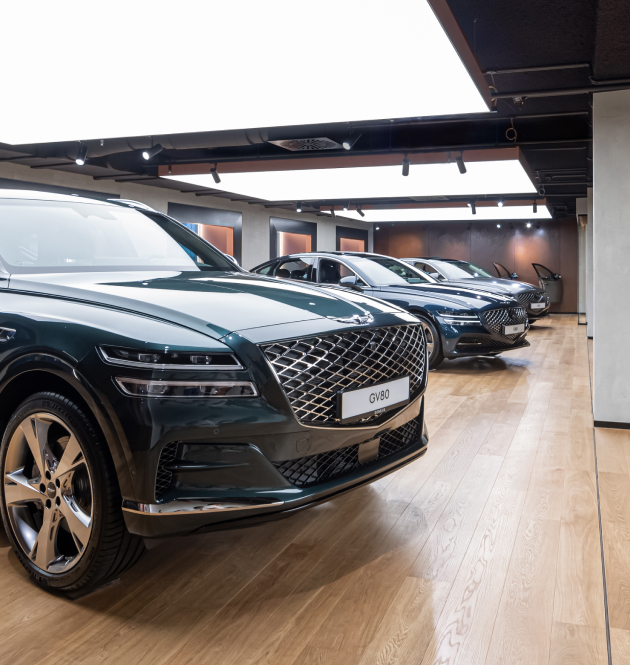 Three Genesis vehicles are lined up under ceiling lighting.