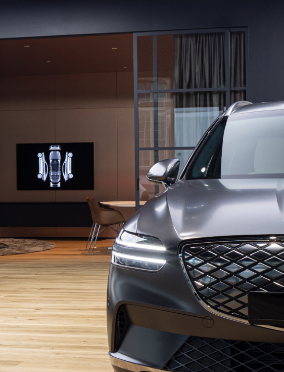 Behind the front view of a Genesis vehicle is a consultation room with a photo hanging on the wall.