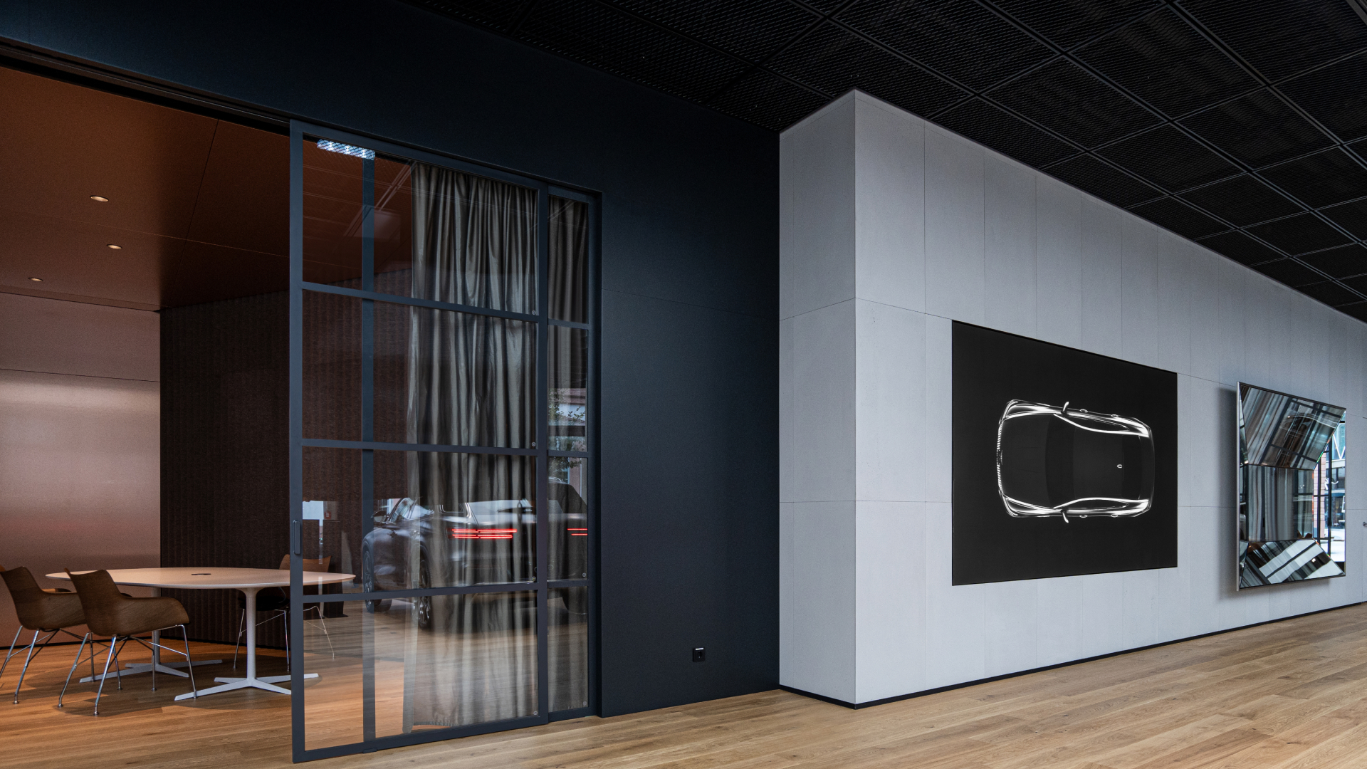 A consultation area is sectioned off behind a glass door. Next to it is a large wall with a photo of a top view outline of a Genesis vehicle and polyhedral mirror.