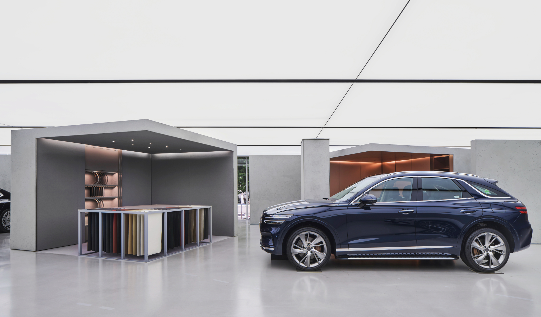 A Genesis vehicle is seen within gray exposed concrete walls. A soft light emits from the ceiling lights.