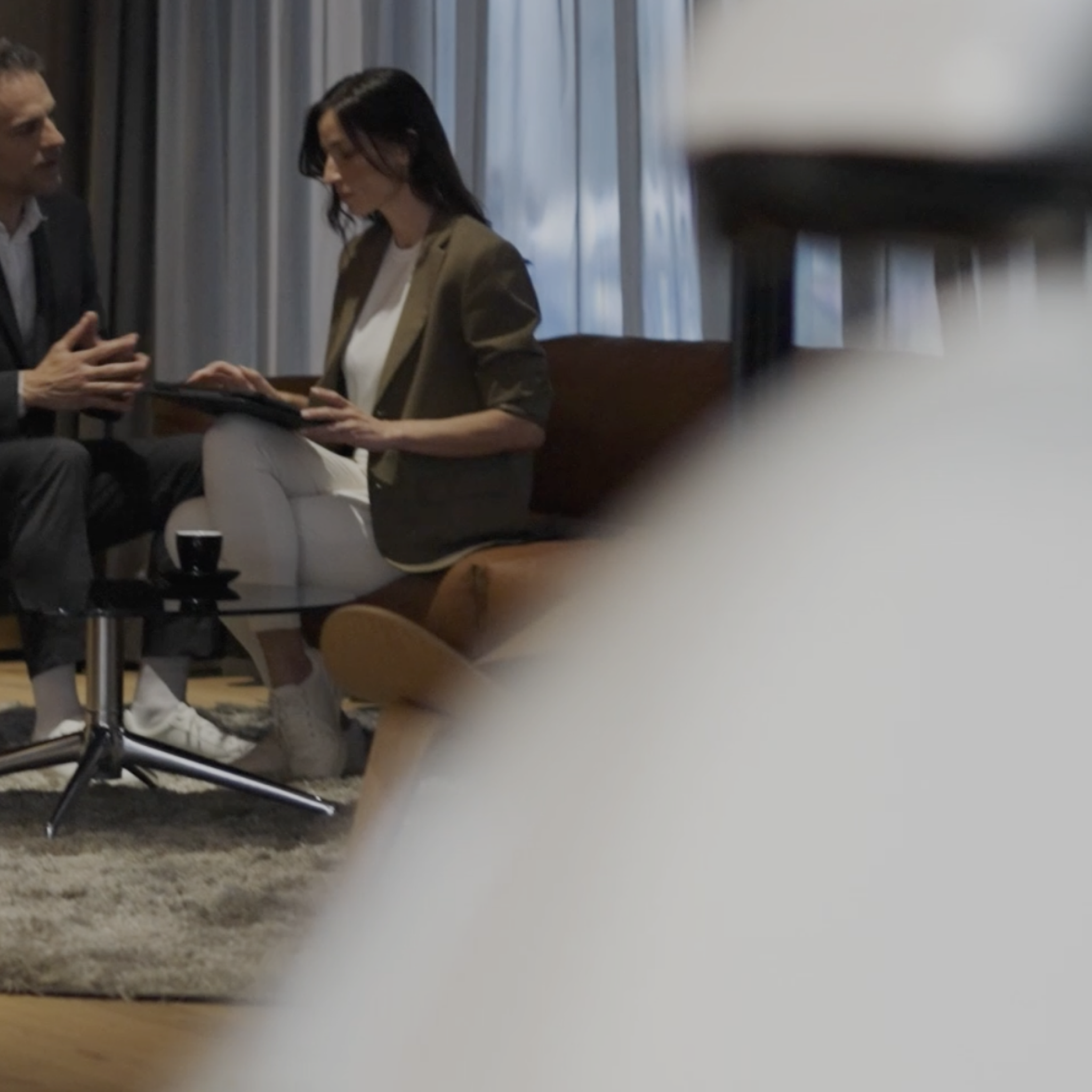 A curator and guest converse while looking at a tablet. They're sitting in a soft-looking space with a rug beneath their feet.